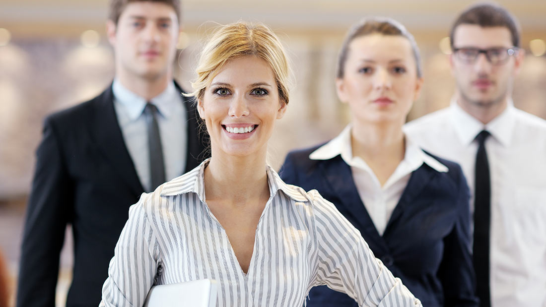 Confident businesswoman smiling with colleagues in background.