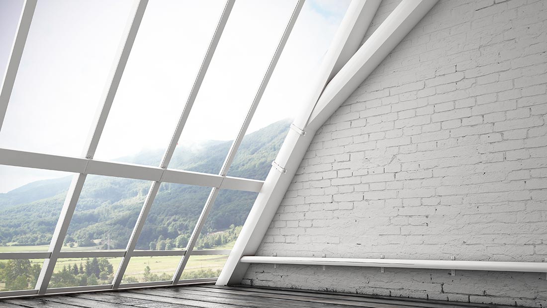 Modern empty room with large slanted windows and mountain view.
