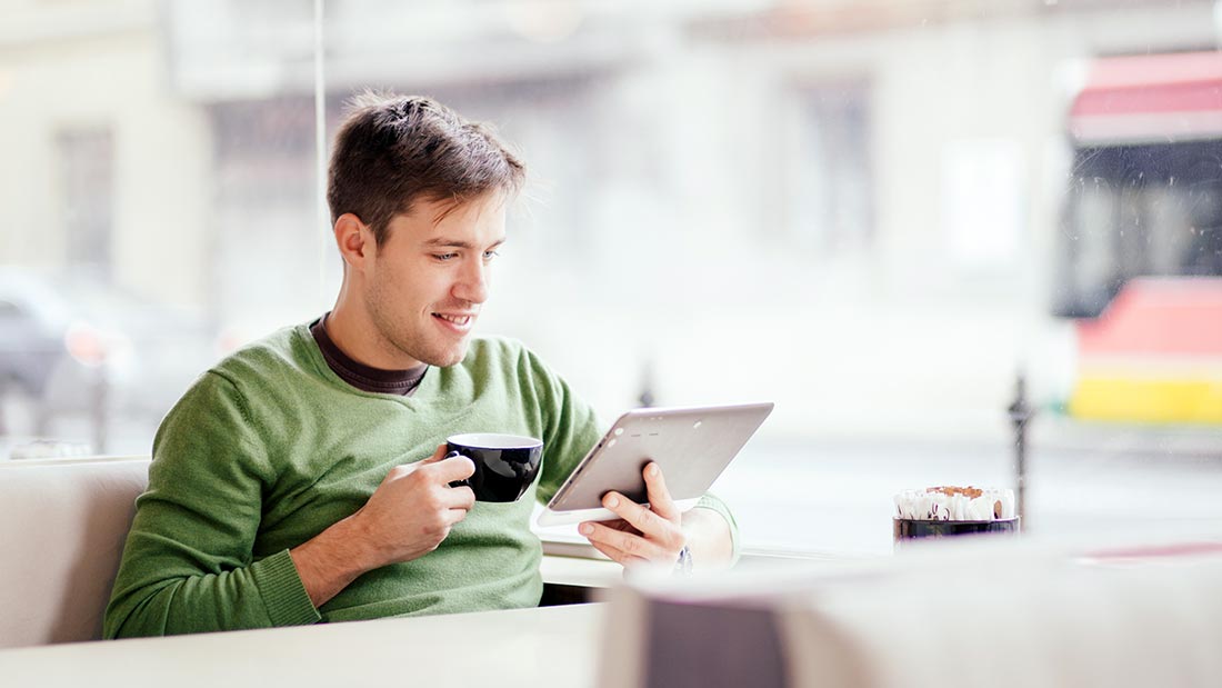 Young man enjoying coffee while reading on a tablet.
