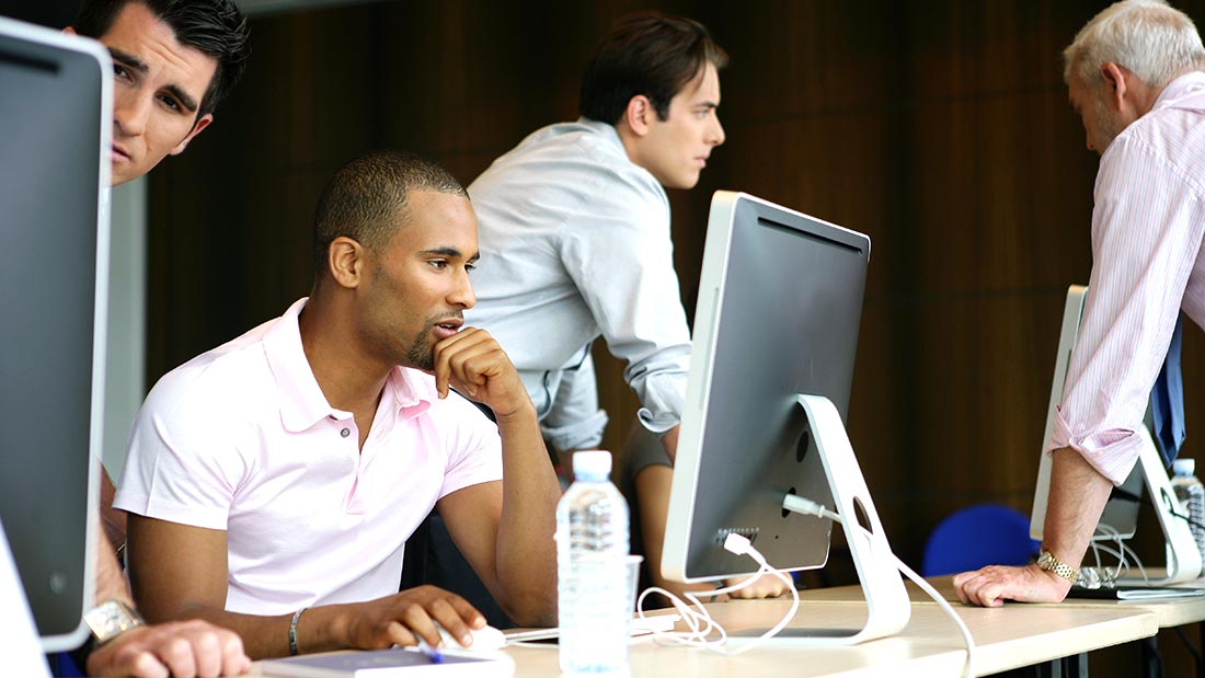 Two men working intently at a computer in an office setting.