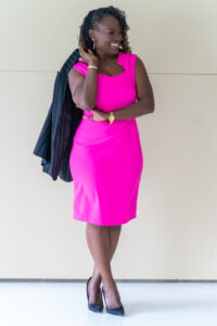 Woman in a bright pink sleeveless dress holding a black jacket.