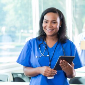 Smiling healthcare professional in blue scrubs holding a tablet.
