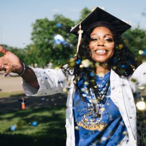 A joyful graduate throws confetti in celebration outdoors.